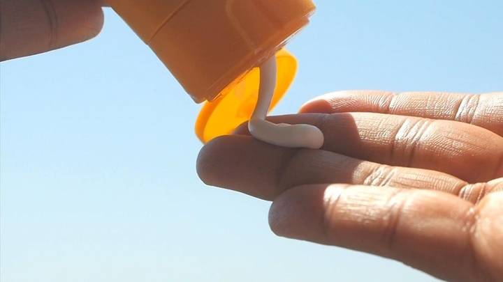 Hand holding sunscreen bottle tilted to show contents against clear sky