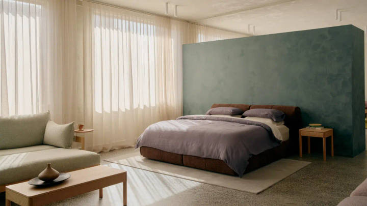 Modern bedroom with brown leather headboard, gray bedding, green accent wall, cream sofa, and natural lighting