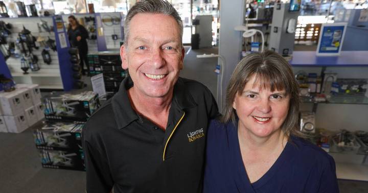 Two smiling people standing in a lighting retail store with fixtures and displays in background