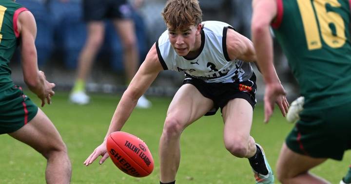 Michael Hughes. Young AFL player in North Ballarat white jersey kicks red football during match