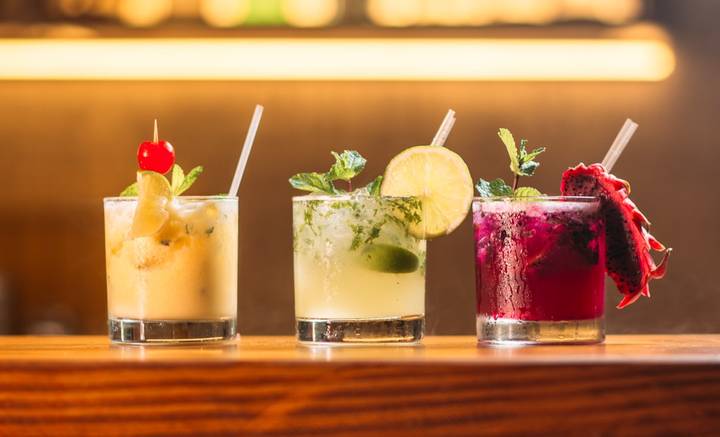 File image: Three professionally crafted cocktails displayed on a bar counter with warm lighting