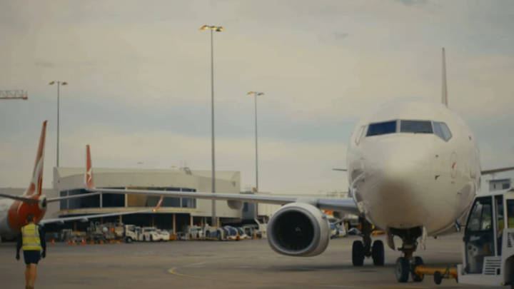 White Qantas aircraft parked at airport terminal with ground support equipment visible