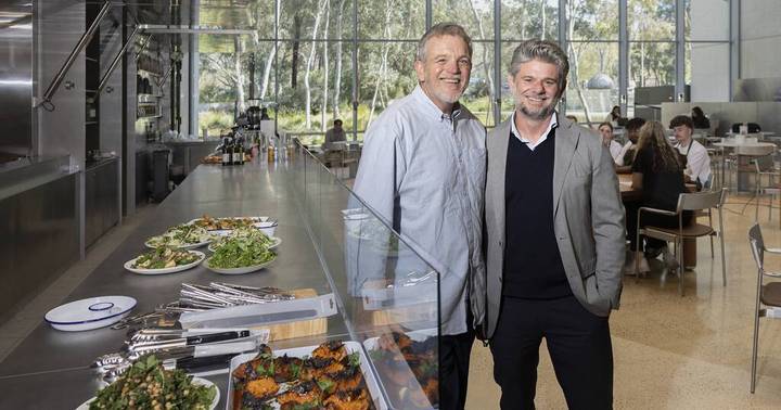 Two men in modern light-filled cafe with counter food display and garden views