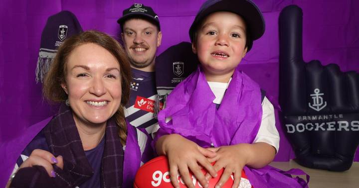 Narelle Rodgers. Woman, young child in purple vest, and two men wearing Fremantle Dockers merchandise at stadium event