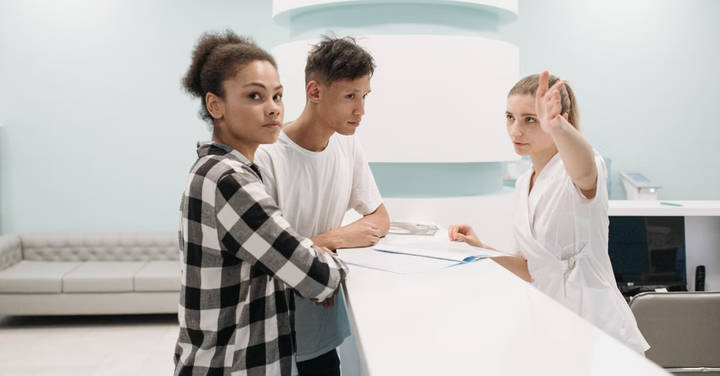 File image: Two people at a service desk receiving assistance from a staff member in a professional setting.