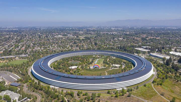 Aerial view of Apple Park, Apple's distinctive circular headquarters building in Cupertino, California, surrounded by green landscaping and trees.