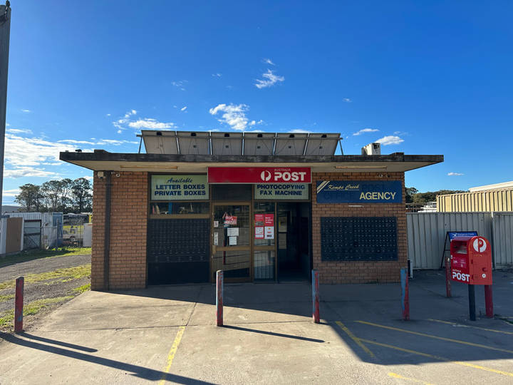 A small weathered brick Australia Post agency building with red and green signage, rows of private letter boxes on the exterior walls, and a red Australia Post mailbox standing out