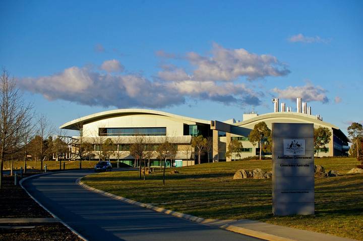 The modern curved headquarters building of Geoscience Australia in Canberra, with the official Australian Government Geoscience Australia sign and coat of arms prominently displaye
