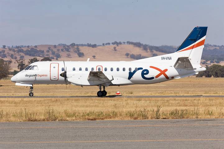 A Regional Express (Rex) Saab 340 turboprop aircraft in white livery with the rex logo and 'Regional Express' branding, parked on a runway apron at a regional Australian airport wi