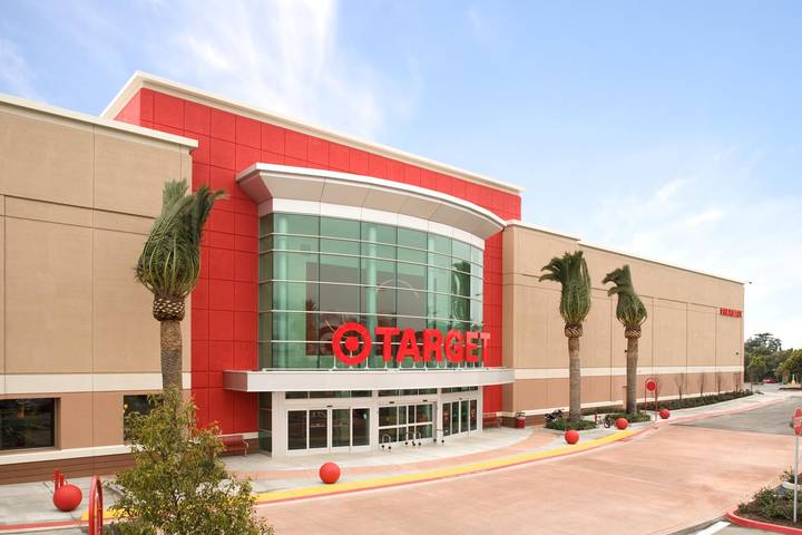 The exterior of a Target retail store with its red and tan facade, large glass entrance, prominent red Target logo and signage, palm trees, and an empty parking area in front.