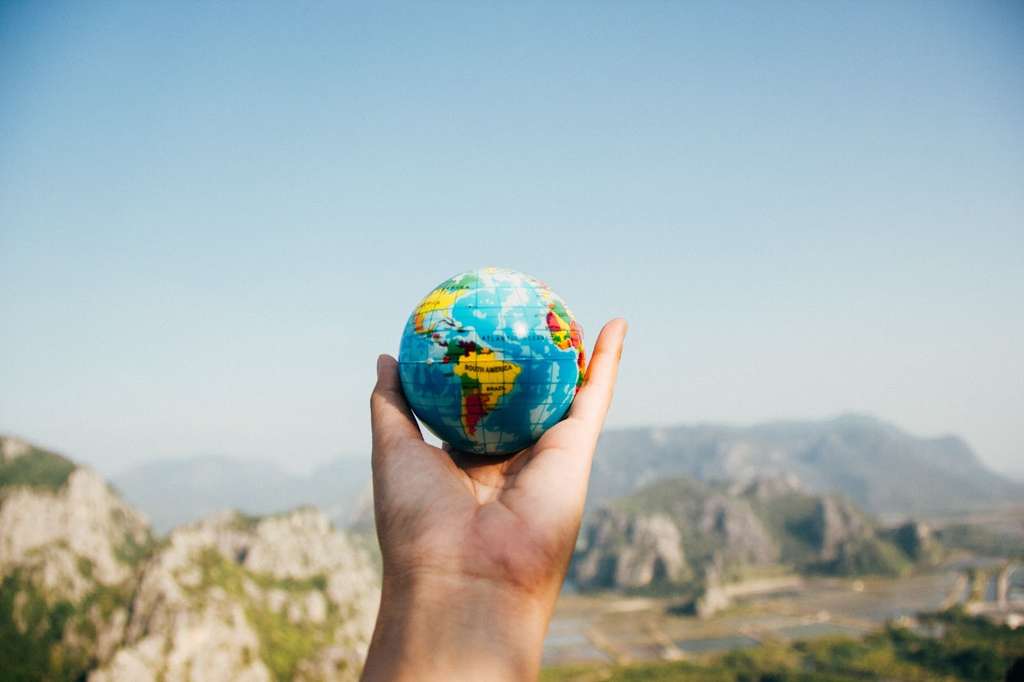 A hand holding a globe with mountains in the background, representing the adventurous spirit of a travel agency.