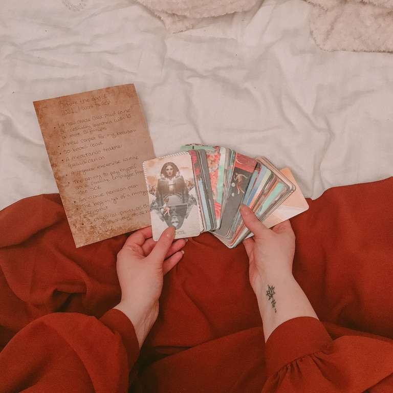 A tarot reader holding tarot cards on a bed.