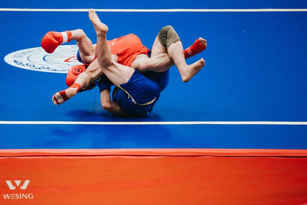 Two men are wrestling on a blue and red court.