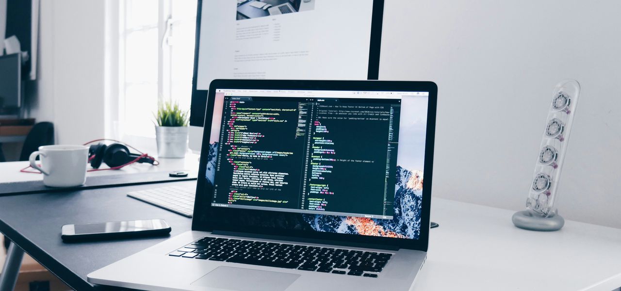 A MacBook with lines of code on its screen on a busy desk