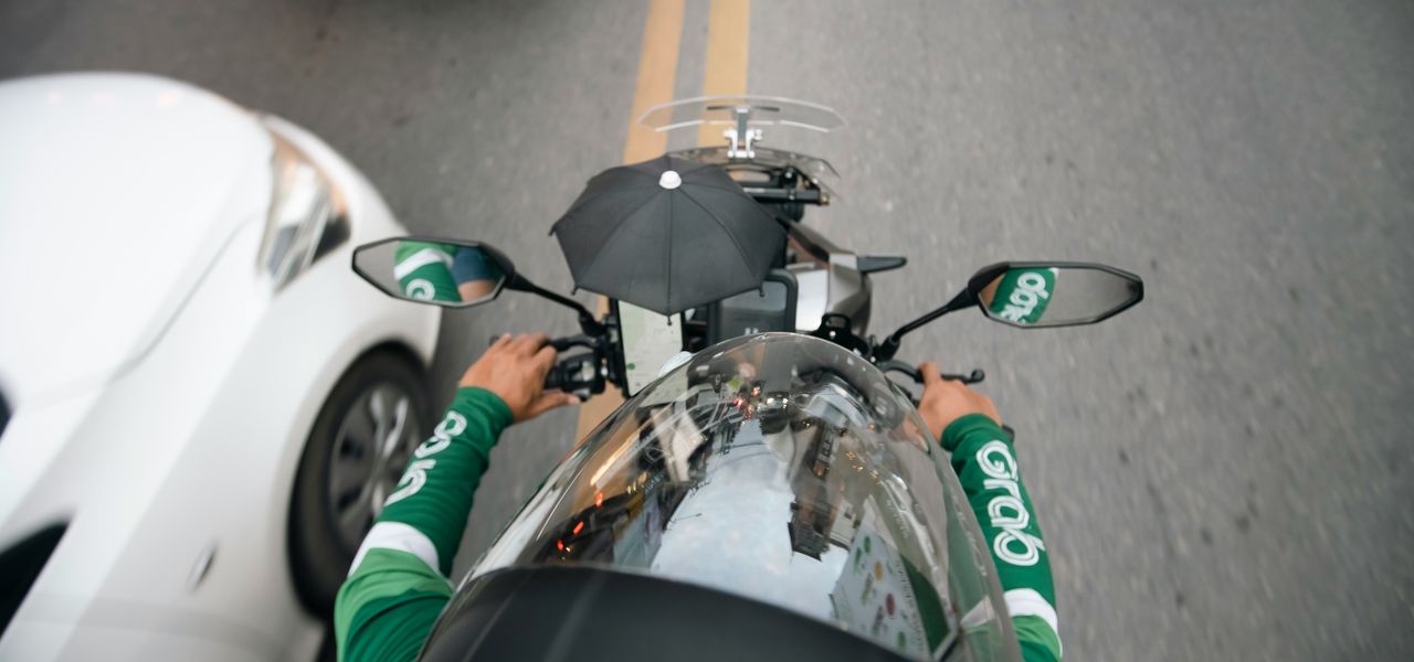 a man riding a motorcycle down a street next to a white car