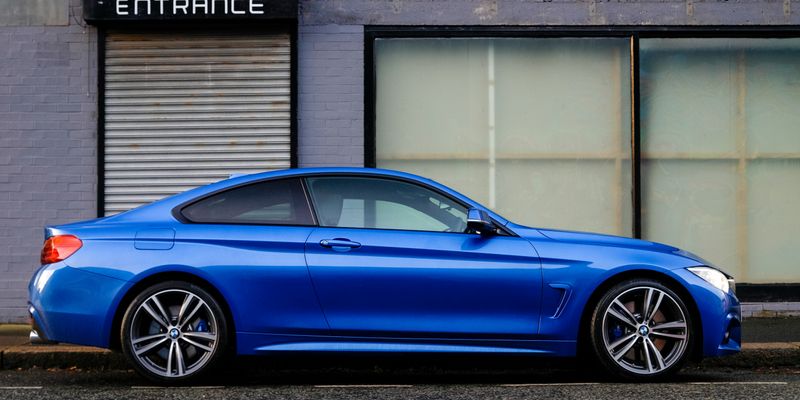 blue coupe beside gray house