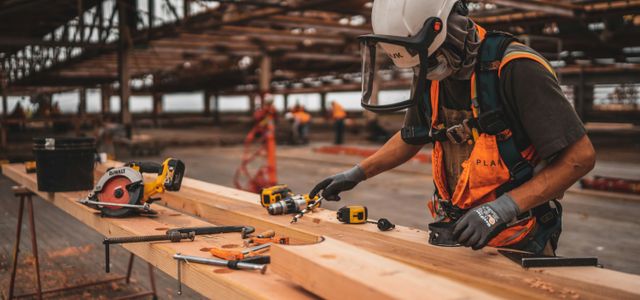 man in orange and black vest wearing white helmet holding yellow and black power tool