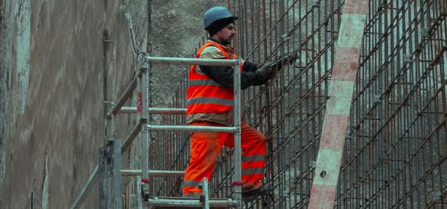 man in red jacket and blue cap standing on ladder