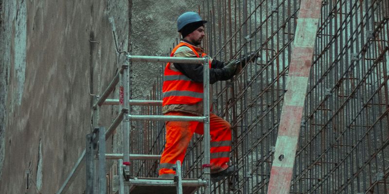 man in red jacket and blue cap standing on ladder