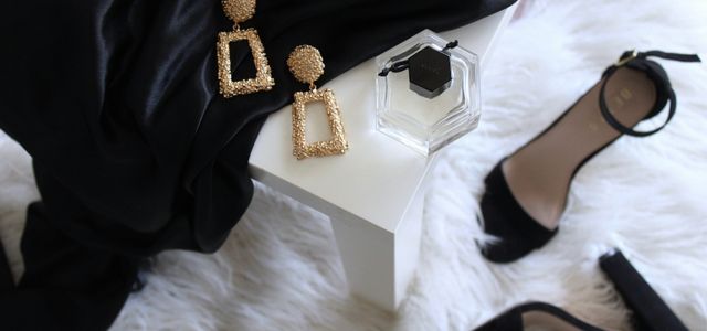 pair of gold-colored earrings on table and black ankle-strap pumps on area rug