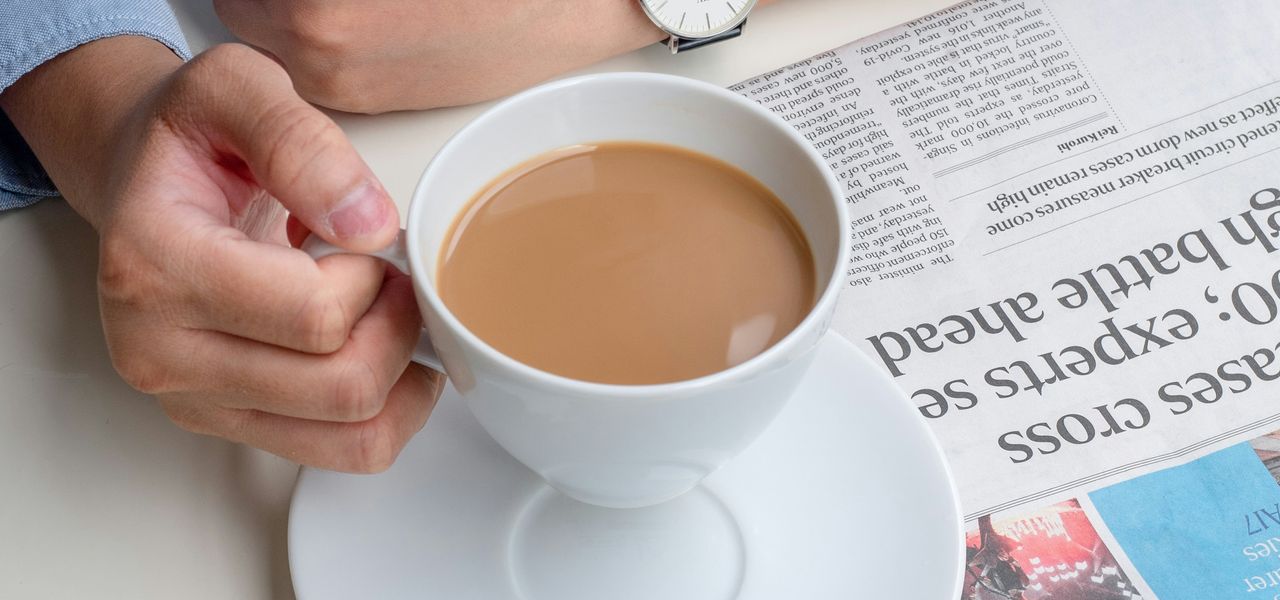 person in blue long sleeve shirt holding white ceramic cup with brown liquid
