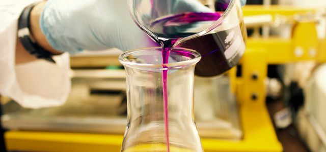person pouring purple liquid on clear glass container