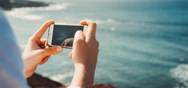 person standing on cliff taking photo of body of water during daytime