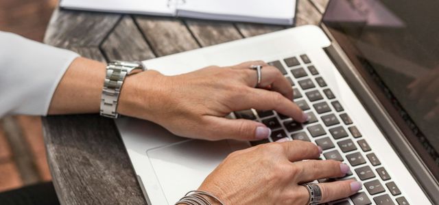 person typing on MacBook Pro on brown wooden table during daytime photo