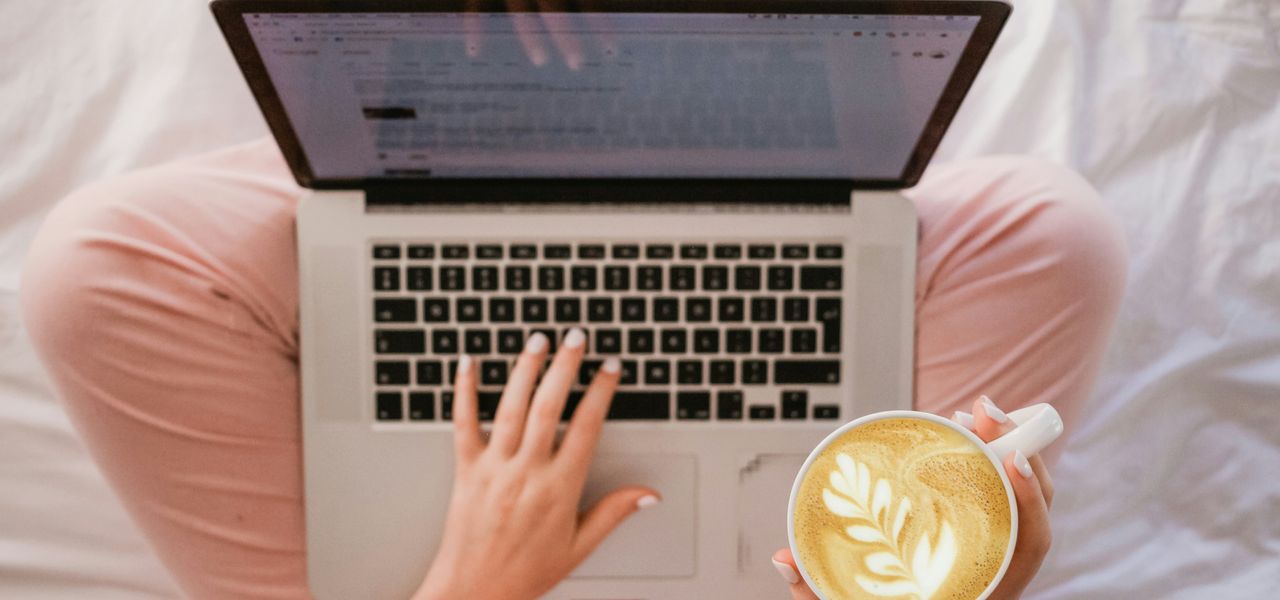 person using MacBook Pro and holding cappuccino