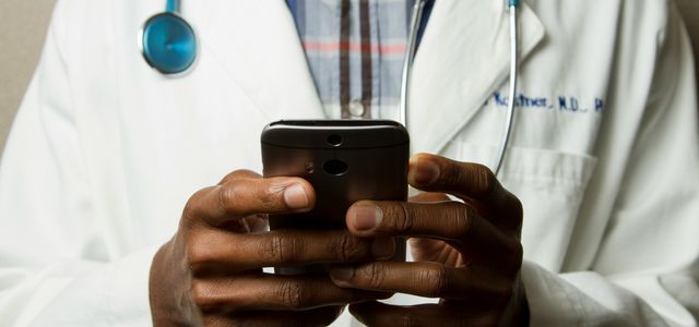person wearing lavatory gown with green stethoscope on neck using phone while standing