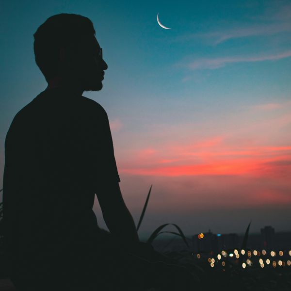 silhouette of man on top of hill overlooking lighted city at dawn