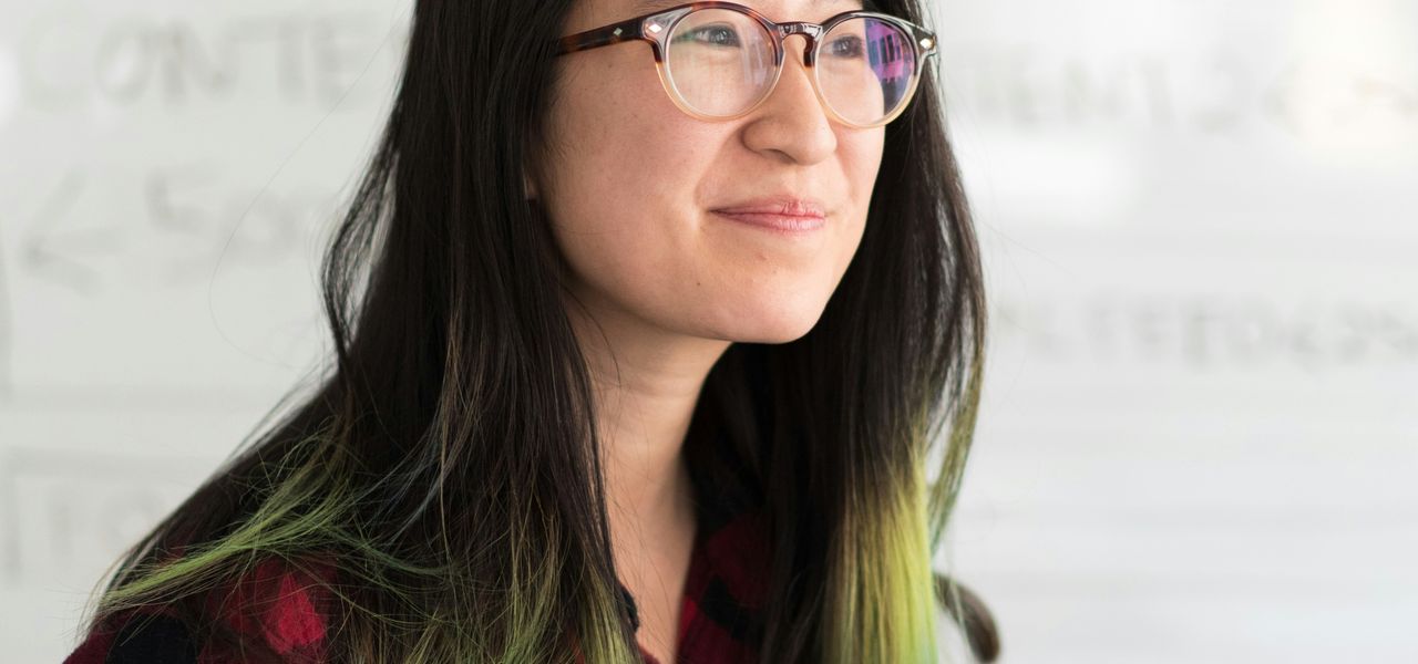 smirking woman wearing red and black checkered top and eyeglasses