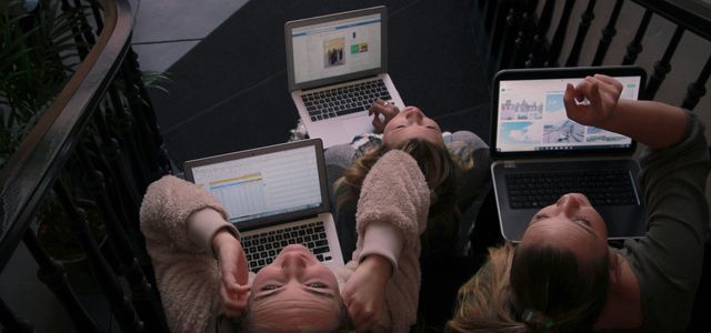 three person using laptops while sitting on ladder