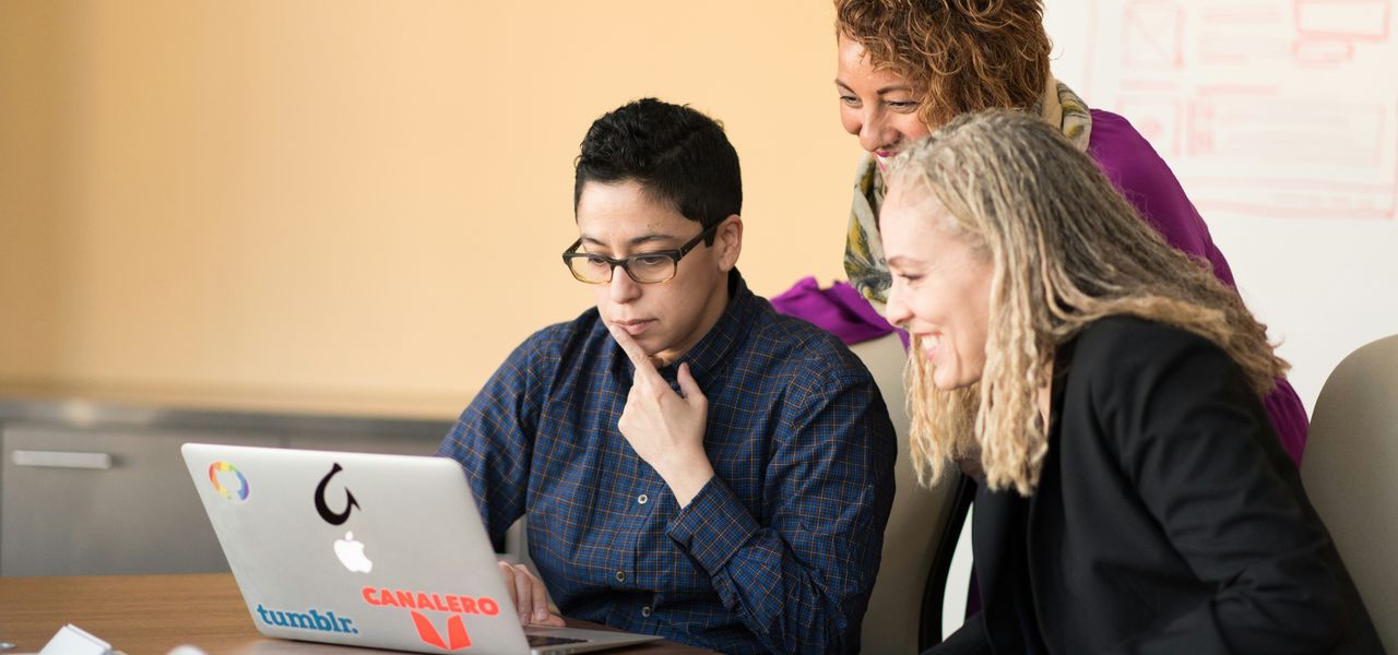 three women beside table looking at MacBook