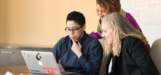 three women beside table looking at MacBook
