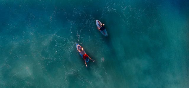 top view photography of two persons on blue surfboard at daytime