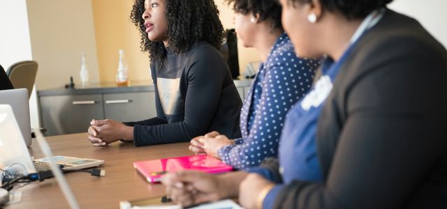 two women sitting at table looking at talking woman