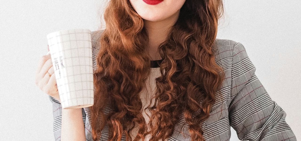 woman in gray cardigan holding white ceramic mug