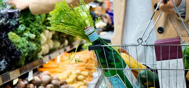 woman in white coat holding green shopping cart