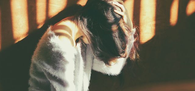 woman leans on wall in white fur jacket docking her head while holding it using her leaf hand