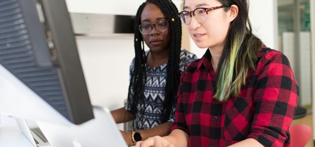 woman wearing red and black checkered blouse using flat screen computer