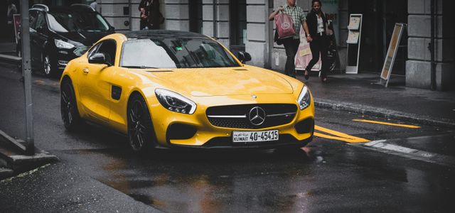 yellow Mercedes-Benz coupe on asphalt road near concrete building