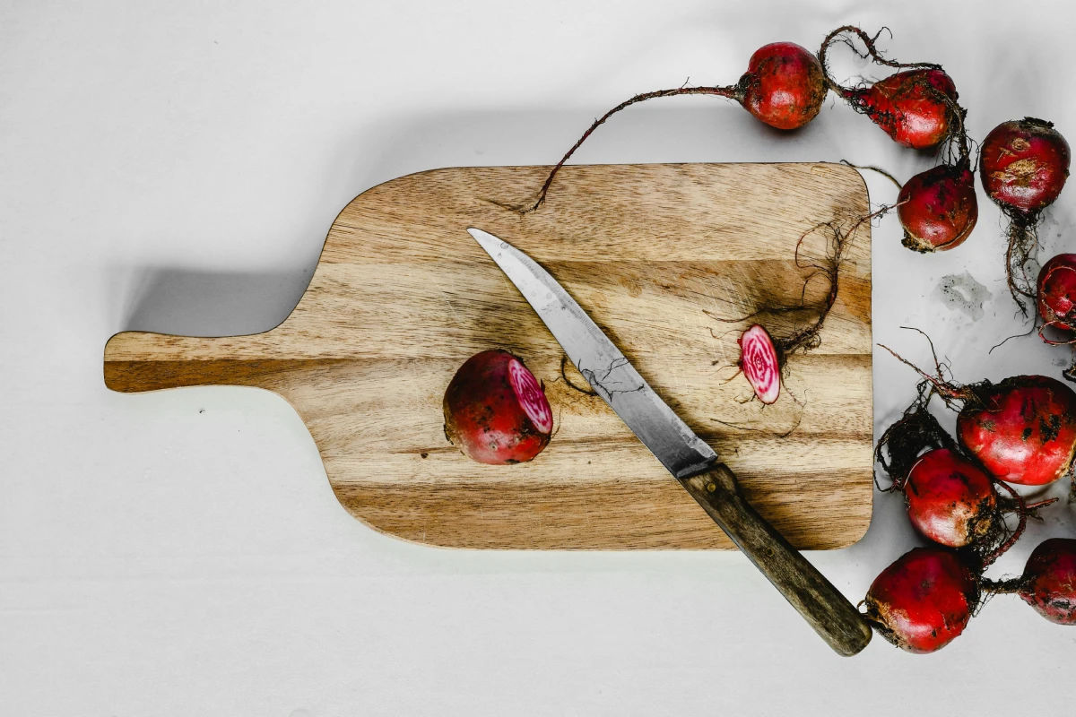 Overhead view of a wooden cutting board with a knife and sliced beetroots, related to beetroot allergy article