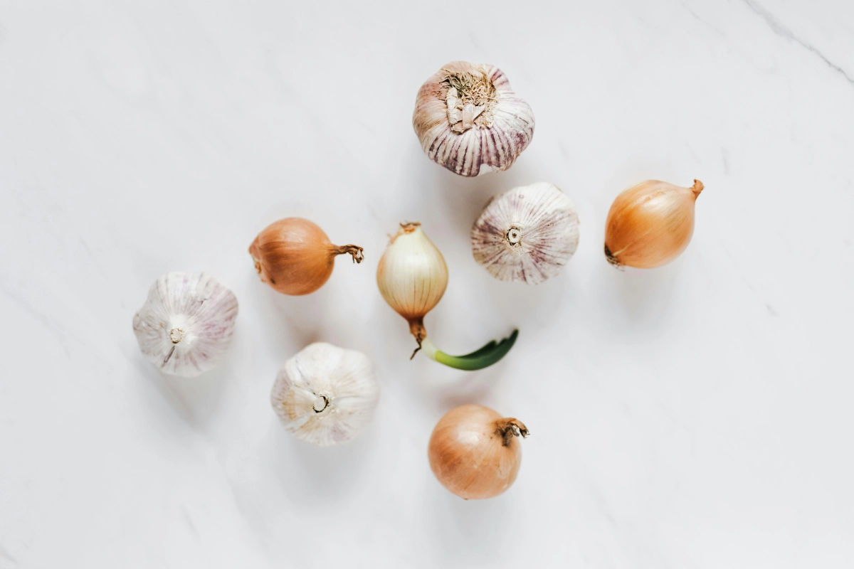 Garlic bulbs and onions on a white marble surface, related to an article discussing garlic and onion allergies.