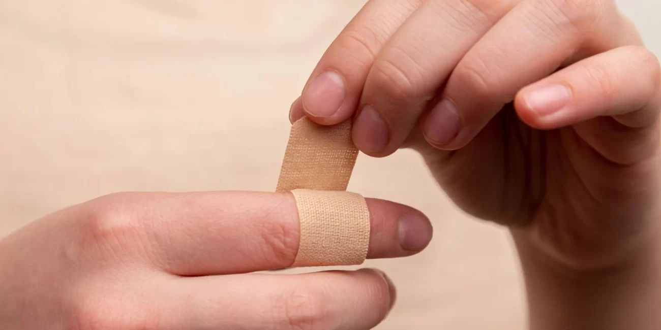 Person applying a band-aid to a finger, showing potential allergic reaction concerns and bandaid alternatives.