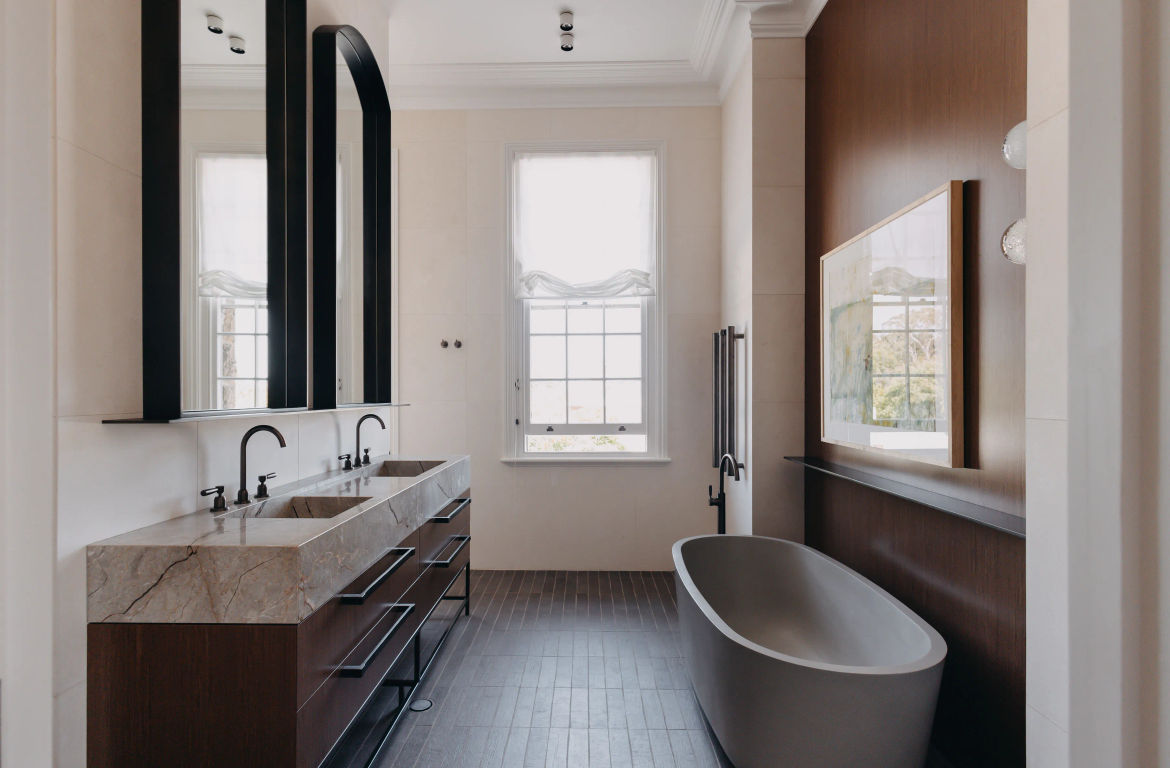 Wide view of bathroom including freestaning bath, double sink vanity, tiled floors and walls