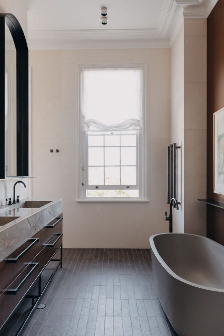 Wide view of bathroom including freestaning bath, double sink vanity, tiled floors and walls