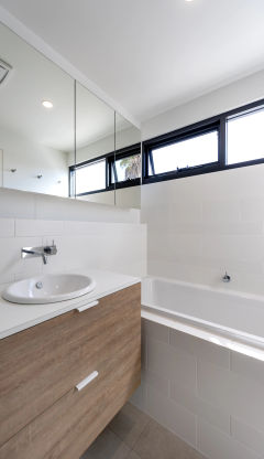 Modern white bathroom with wooden cabinets with white tiling on the walls.