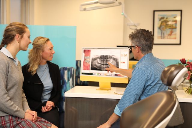 Orthodontist consulting with parent and teeanager on computer