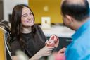 female patient smiling at dentist holding model teeth